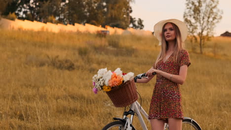 Zeitlupe,-Sexy,-Schöne-Frau-Mit-Einem-Fahrrad,-Einem-Hut-Und-Einem-Leichten-Sommerkleid-Kommt-Mit-Blumen-In-Einem-Korb-Und-Lächelt.